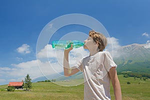 Teenager boy drinking clear water from battle in his hands high in Alps