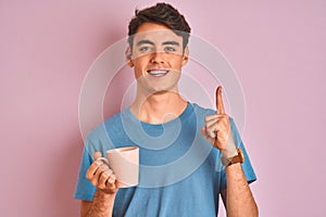 Teenager boy drinking a cup of coffee over isolated pink background surprised with an idea or question pointing finger with happy