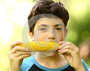 Teenager boy eating boiled corn cob close up photo