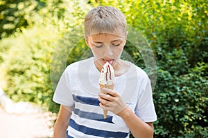 Teenager boy eating ice-cream cone on green nature background. Summer, junk food and people concept