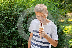 Teenager boy eating ice-cream cone on green nature background. Summer, junk food and people concept