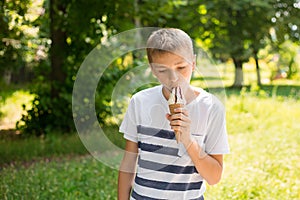 Teenager boy eating ice-cream cone on green nature background. Summer, junk food and people concept. Copyspace