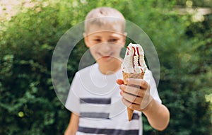 Teenager boy eating ice-cream cone on green nature background. Summer, junk food and people concept. Focus on hand