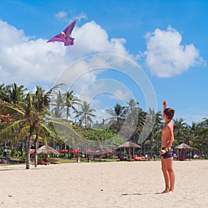 Teenager boy flying a kite on tropical beach