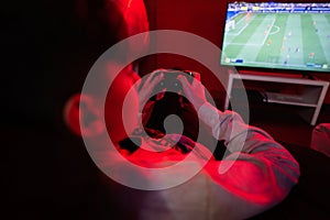 Teenager boy gamer play football gamepad video game console in red gaming room