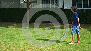 A teenager boy and girl play badminton on a green lawn in the backyard of their home