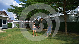 A teenager boy and girl play badminton on a green lawn in the backyard of their home