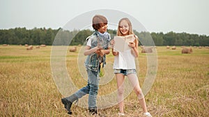 Teenager boy and girl reading book on harvesting field on haystack landscape. Happy girl and boy looking book on