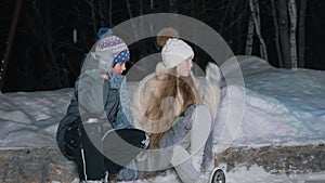 Teenager boy and girl resting after skating on ice rink at winter evening in park. Girl and boy in skates sitting in