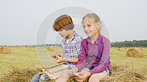 Teenager boy and girl sitting on haystack at countryside field. Carefree boy and girl reading book on hay stack at
