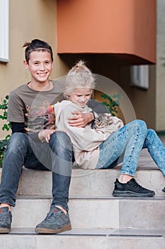 Teenager boy and girl sitting near house during walk talking and petting kitten