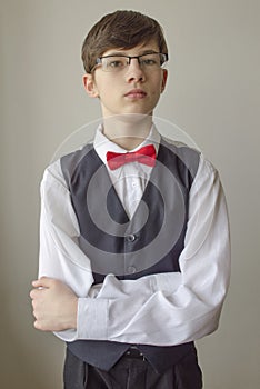 Teenager boy with glasses in a white shirt and a waistcoat with the red bow tie