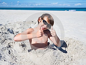 Teenager boy has fun digging in the sand at Baltic Sea