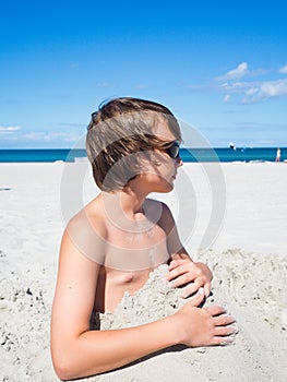 Teenager boy has fun digging in the sand at Baltic Sea