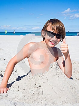 Teenager boy has fun digging in the sand at Baltic Sea