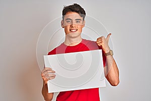 Teenager boy holding advertising banner with blank space over isolated background happy with big smile doing ok sign, thumb up