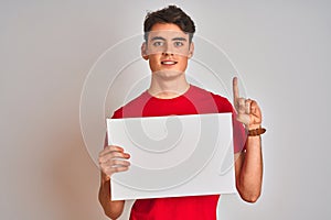 Teenager boy holding advertising banner with blank space over isolated background surprised with an idea or question pointing