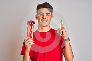Teenager boy holding birthday gift over isolated background surprised with an idea or question pointing finger with happy face,