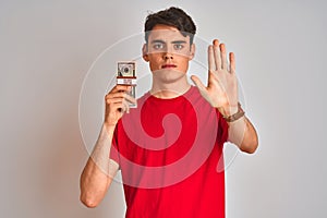 Teenager boy holding a bunch of dollars bank notes over isolated background with open hand doing stop sign with serious and