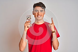 Teenager boy holding a bunch of dollars bank notes over isolated background surprised with an idea or question pointing finger