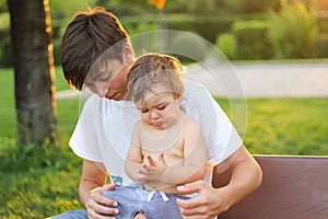 Teenager boy holding his crying little brother on his khees trying to comfort him