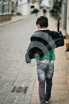 Teenager boy in hoodie and leather jacket walks away on city street