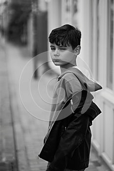 Teenager boy in hoodie and leather jacket walks away on the city street and turns around. Black and white image