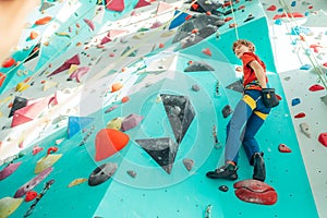 Teenager boy at indoor climbing with top rope on wall hall. Boy is climbing using climbing harness and chalk powder when somebody