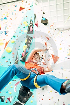 Teenager boy at indoor climbing wall hall. Boy is climbing using an auto belay system and climbing harness. Active teenager time