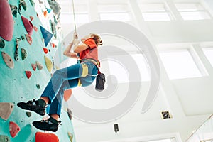 Teenager boy at indoor climbing wall hall. Boy is climbing using a top rope,chalk bag and climbing harness. Active teenager time
