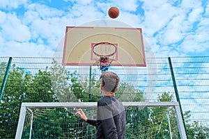 Teenager boy jumping with ball playing street basketball, back view