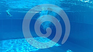 Teenager boy jumping into an outdoor pool from a high diving tower  and swimming in cloud of bubbles