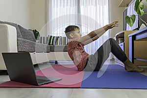 Teenager boy with laptop computer doing sport exercises, practicing yoga in the living room. Sport, healhty lifestyle