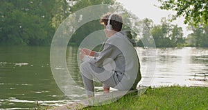 Teenager boy listening relaxing music on headphones while sitting on park