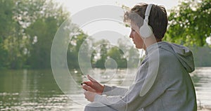 Teenager boy listening relaxing music on headphones while sitting on park