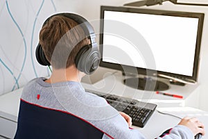 Teenager boy wearing earphones looking at computer monitor. computer screen mockup.