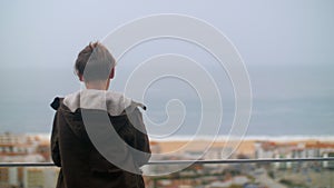 Teenager boy looking at ocean from the hotel on the coast in Nazare, Portugal