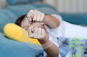 Teenager boy lying on sofa at home showing fig to parents at camera. Teen rudeness and protest.