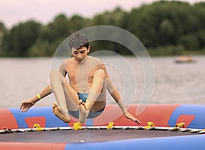 Teenager boy in open air amusement aquapark jump on trampoline