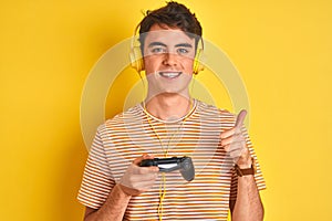 Teenager boy playing video games using gamepad over isolated yellow background happy with big smile doing ok sign, thumb up with