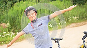 Teenager boy in protective helmet spread his arms out like a bird standing next to his bike in park on summer day