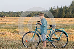 Teenager boy pushing bicycle in farm field