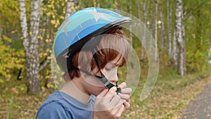 Teenager boy putting bicycle helmet on head in autumn park. Handsome boy wearing blue protective helmet for