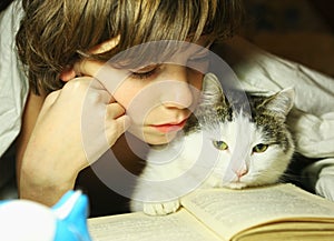 Teenager boy reading book with cat in bed