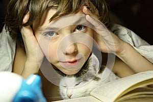 Teenager boy reading book with cat in bed