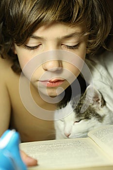 Teenager boy reading book with cat in bed