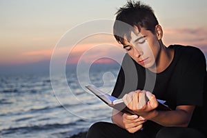 Teenager boy reads book sitting on beach