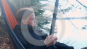 Teenager boy relaxing lying in hammock eating sausage in forest on nature.