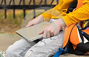 Teenager boy resting in a park after school. Holding a laptop on a sunny day, outdoors.