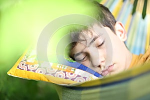 Teenager boy resting sleep with book in hammock on summer green garden